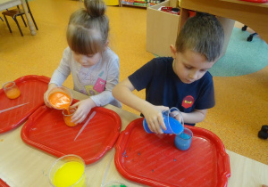 Dwoje dzieci dolewa zabarwioną ciecz do swoich słoiczków.